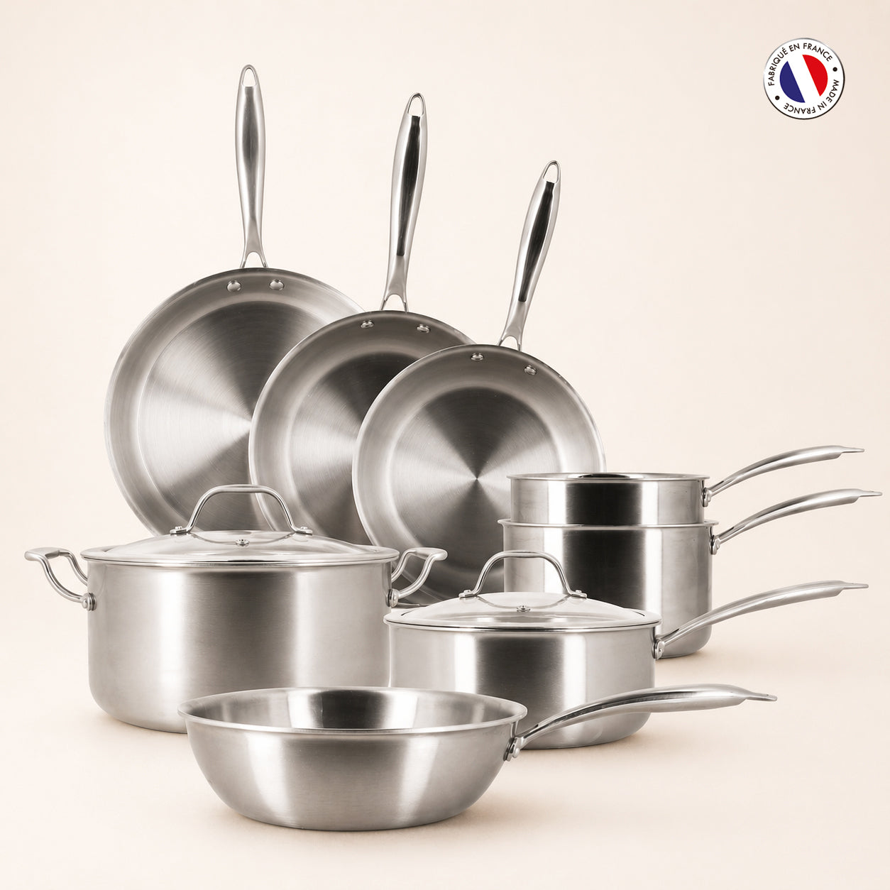 Set de 8 pièces Triply Menastyl en acier inoxydable, poêles casseroles et faitouts disposés sur fond beige