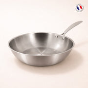 Wok Triply 24cm en acier inoxydable triple couche Menastyl, vue de trois quarts sur fond beige clair