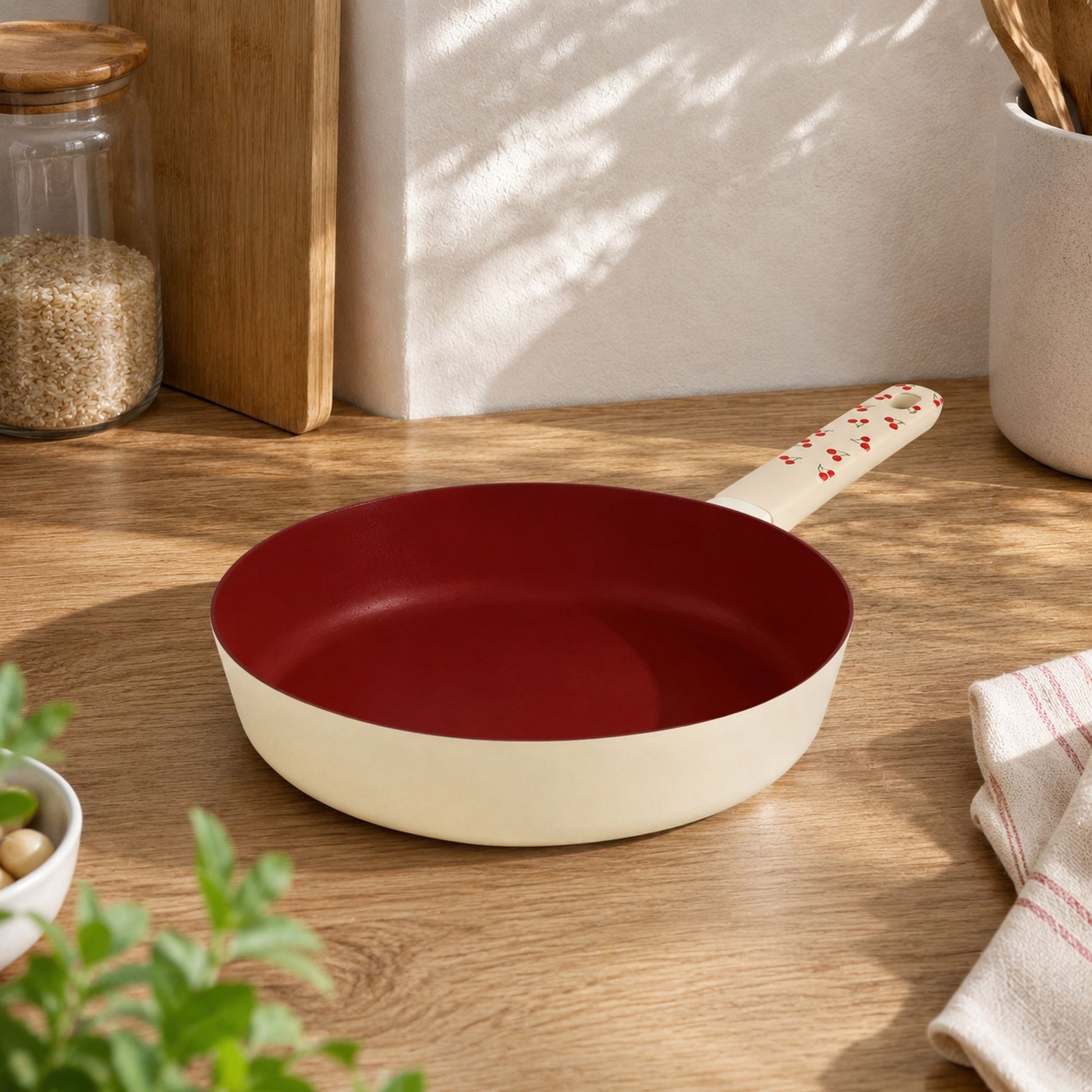 Poêle Cerise 20cm en aluminium couleur crème, intérieur antiadhésif bordeaux, posée sur plan de travail bois clair