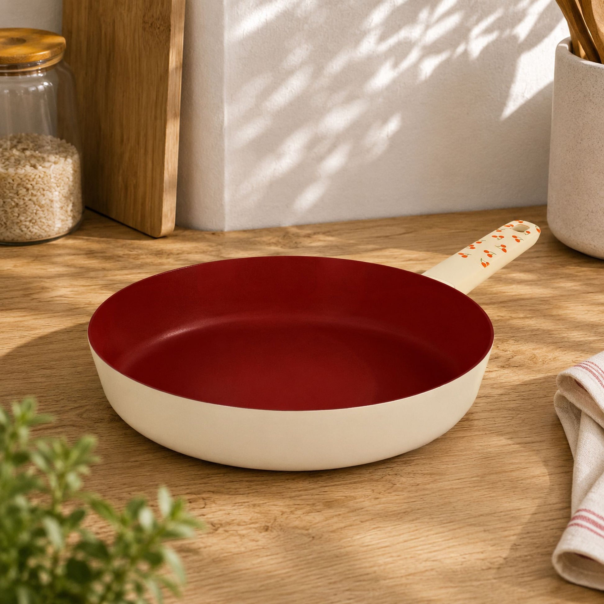 Poêle Cerise 28cm en aluminium crème et rouge bordeaux, posée sur plan de travail bois clair dans cuisine moderne
