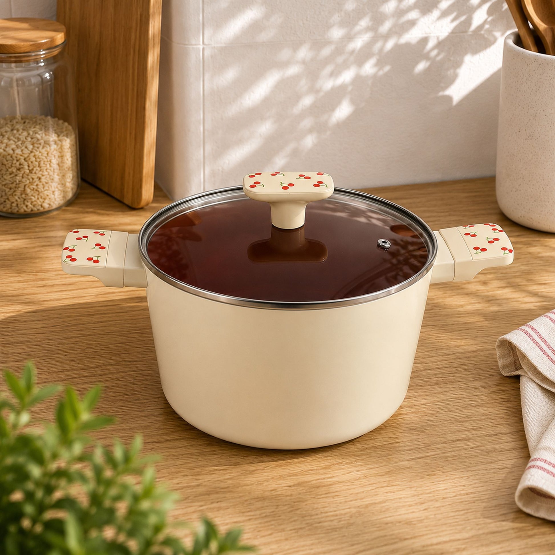Faitout cerise 24cm en aluminium crème avec couvercle en verre, posé sur plan de travail bois clair