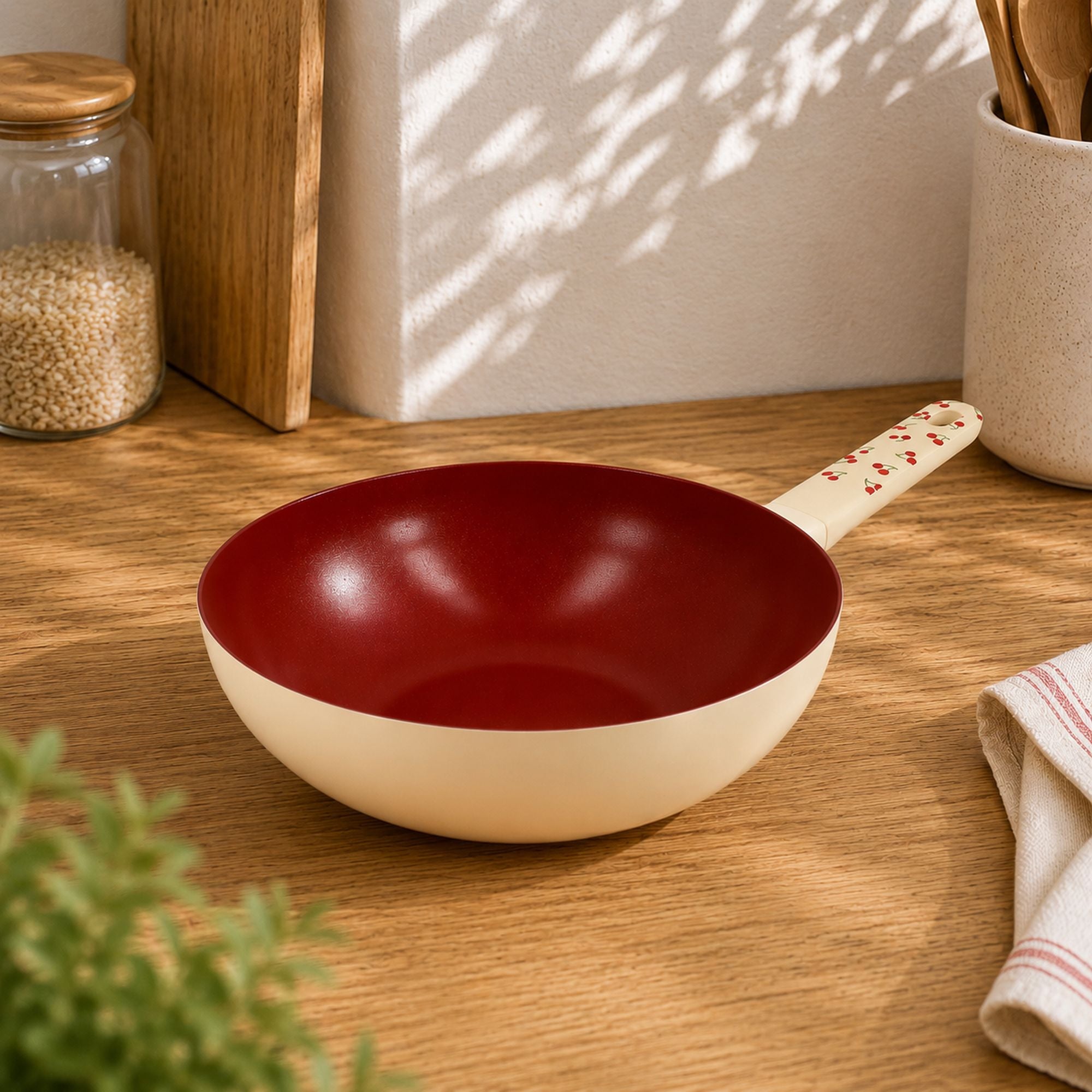 Wok cerise 28cm en aluminium avec intérieur rouge bordeaux et manche assorti, posé sur plan de travail bois clair