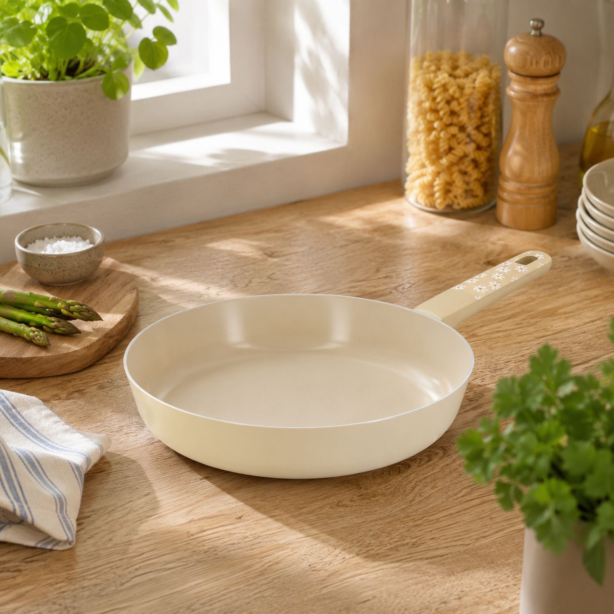 Poêle Marguerite 28cm beige en aluminium avec manche bois décoré, posée sur plan de travail cuisine naturelle avec aspérges fraîches