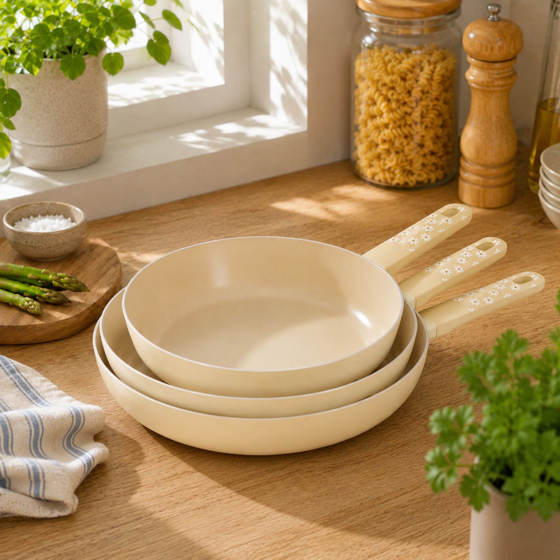 Set de 3 poêles Marguerite 28cm aluminium beige empilées sur plan de travail bois avec ustensiles cuisine