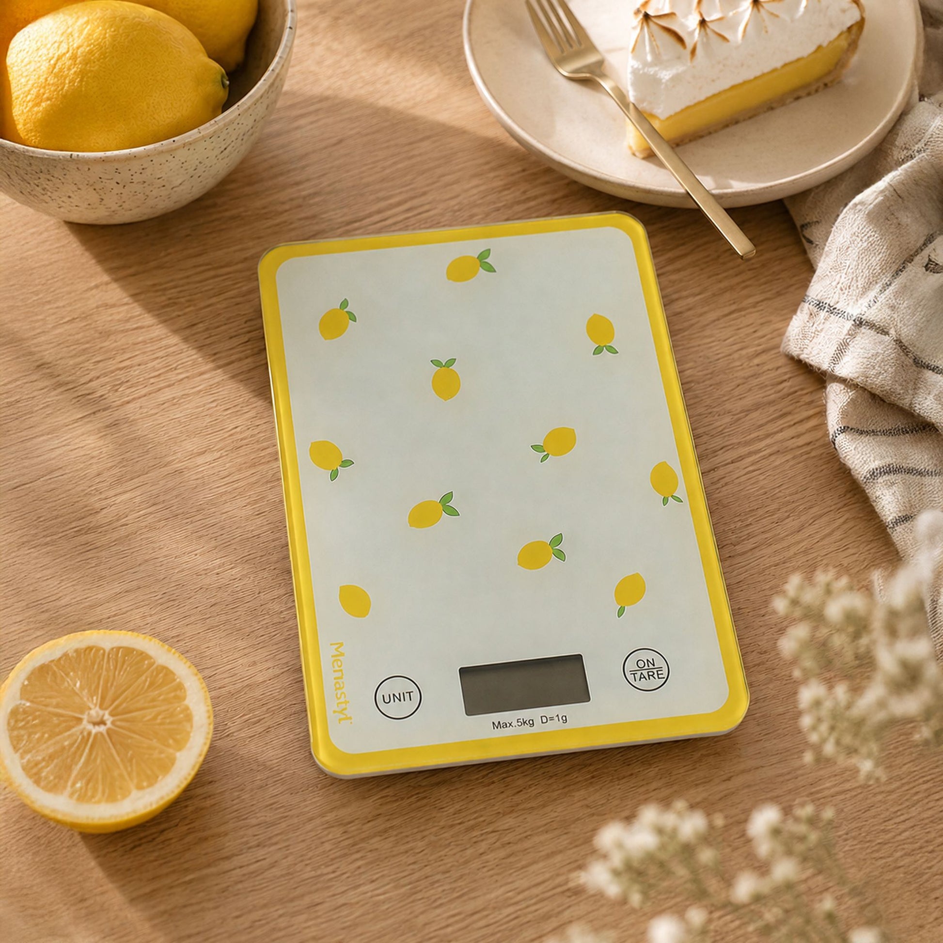 Balance de cuisine électronique motif citron jaune sur table en bois, entourée de citrons frais et tarte meringuée