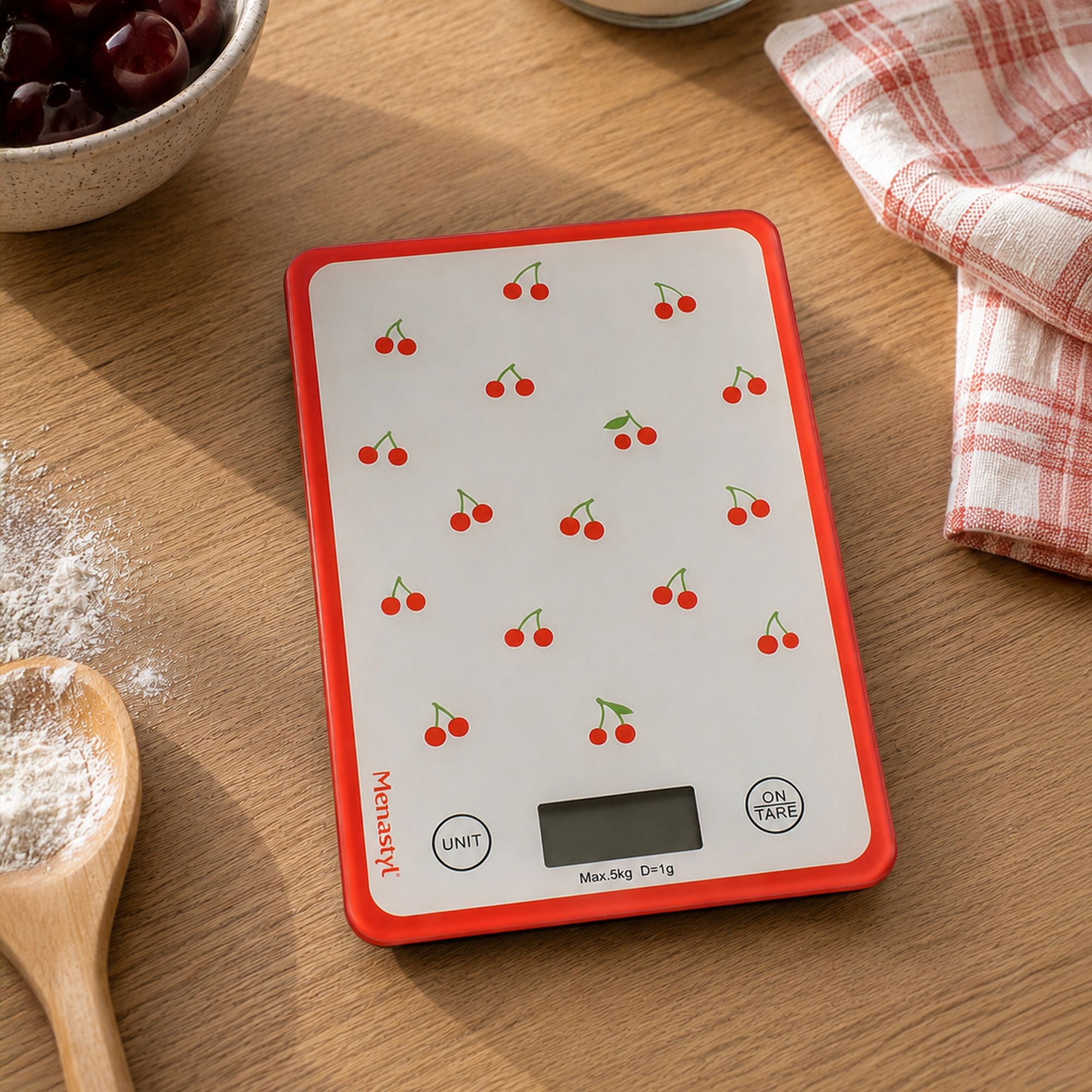 Balance de cuisine électronique à motif cerises rouges, posée sur plan de travail en bois avec bol de fruits