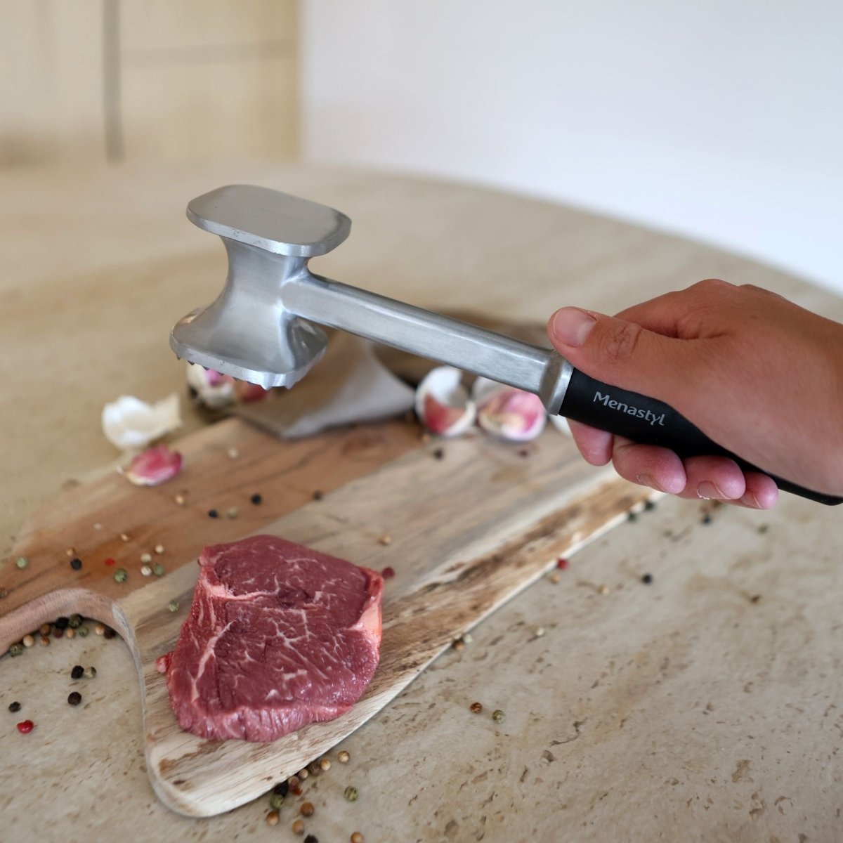 Main tenant l'attendrisseur de viande en aluminium Menastyl face picots au-dessus d'un steak sur planche bois