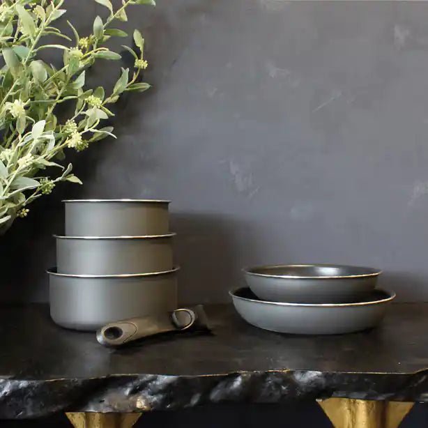 Batterie de cuisine 8 pièces Iris en aluminium gris, casseroles empilées et poêles posées sur plan de travail sombre