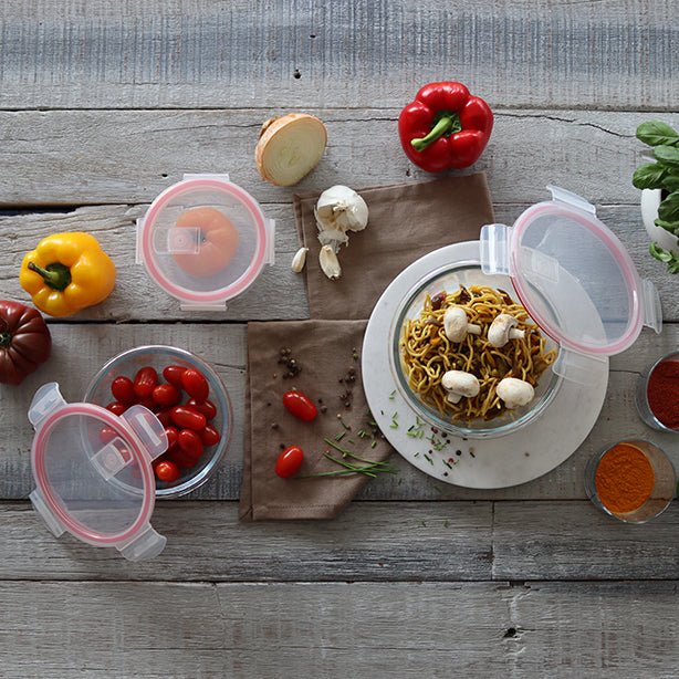 Vue d'ensemble boîtes hermétiques rondes en verre avec couvercles roses, remplies de légumes et pâtes sur table en bois rustique