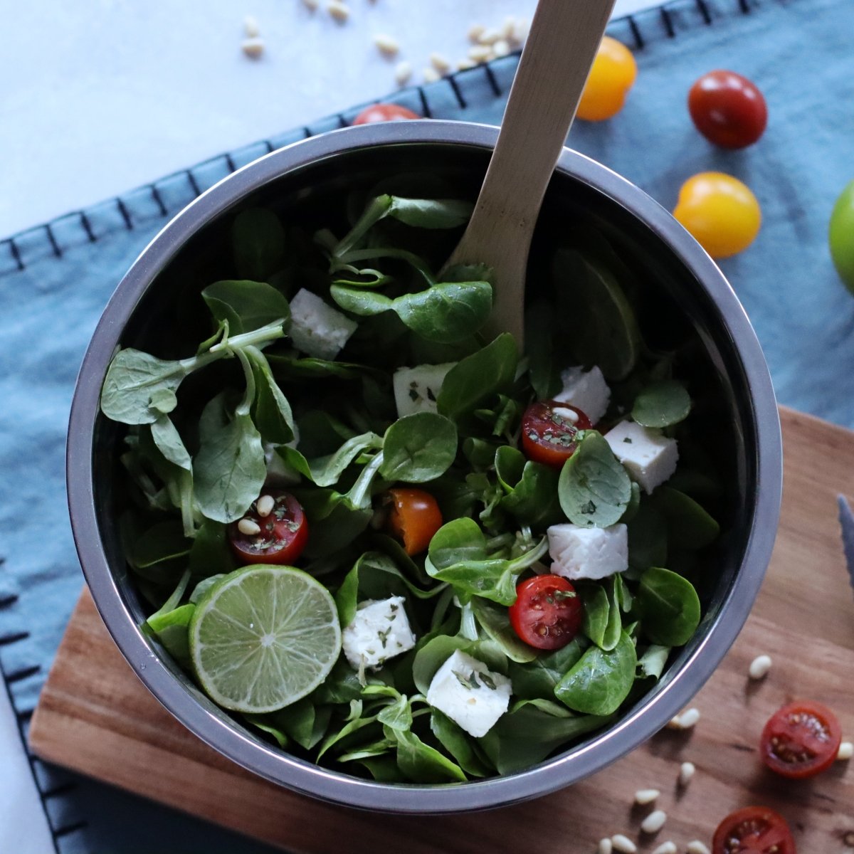 Bol à mélanger inox 25cm avec salade verte, tomates cerises et feta, vue de dessus sur planche bois