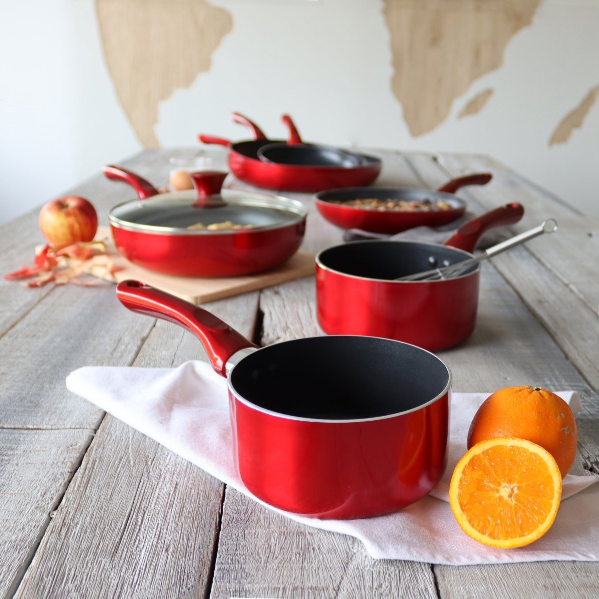 Collection casseroles Cerise rouges avec intérieur antiadhésif noir sur table en bois rustique, orange en premier plan