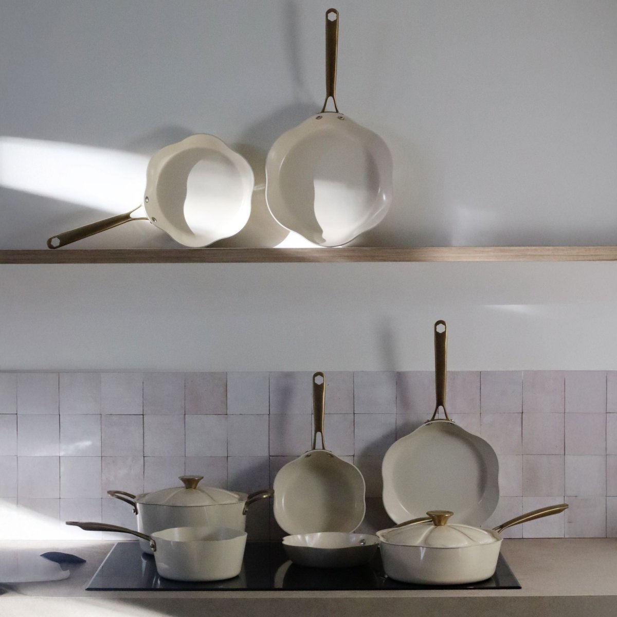 Casseroles Dahlia beige en aluminium recyclé disposées sur étagère en bois et plaque de cuisson induction