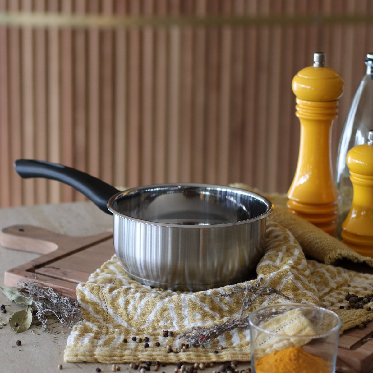 Casserole First 16 cm en acier inoxydable avec poignée noire, posée sur tissu jaune avec huile et épices