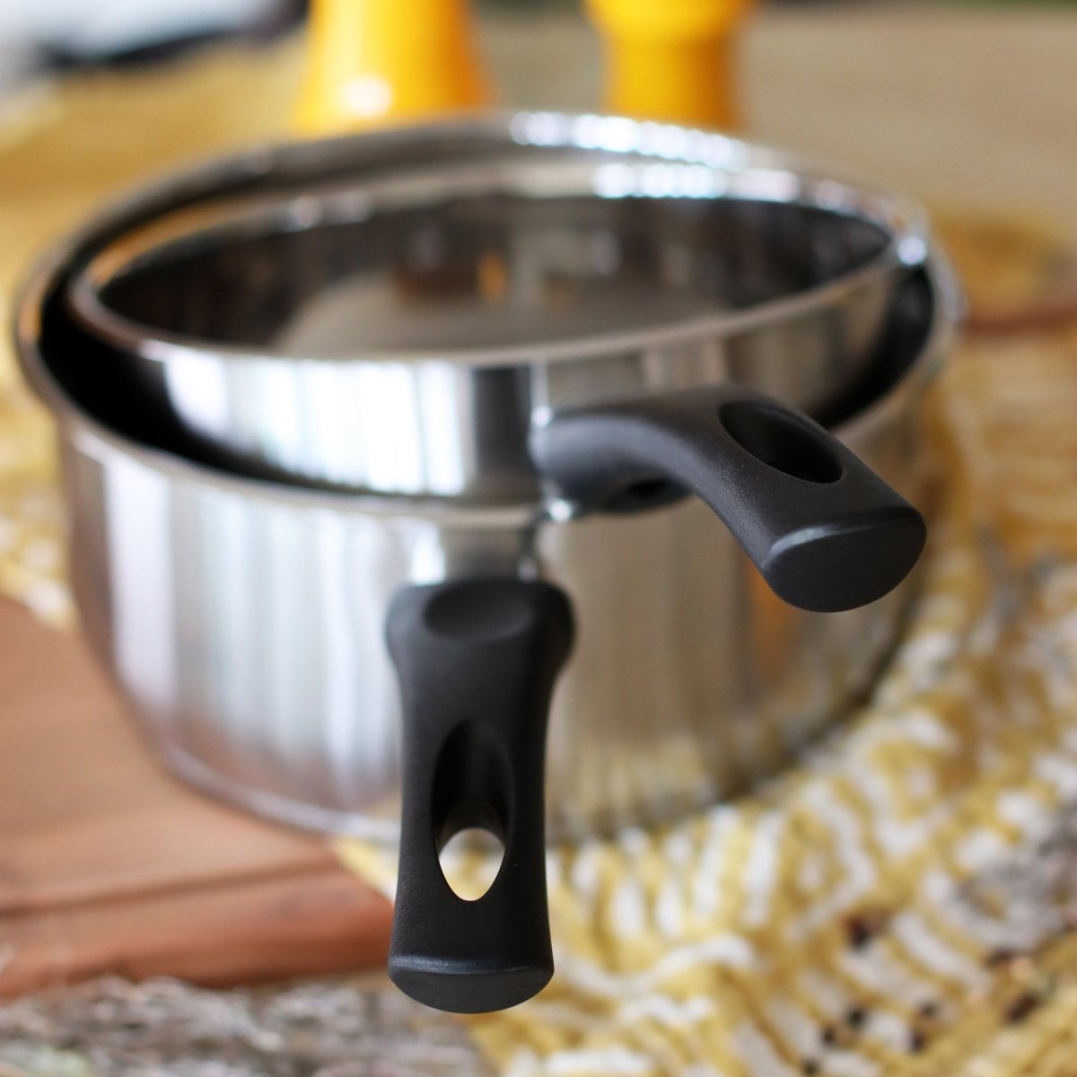 Casserole First 16cm en acier inoxydable avec poignées noires, vue de détail sur plan de travail bois