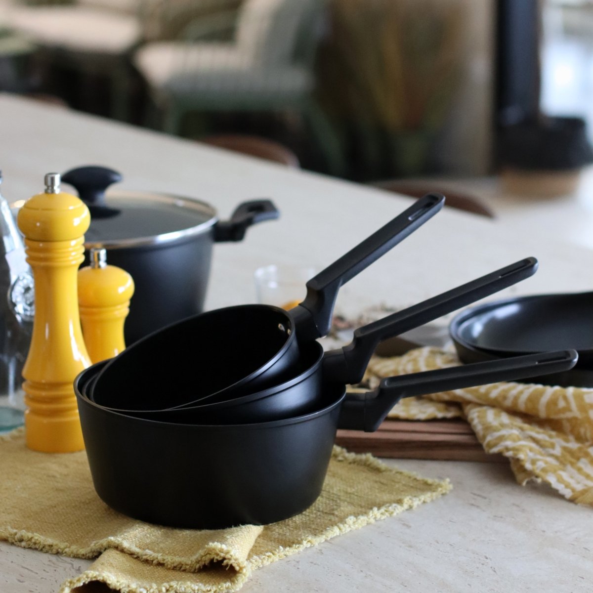 Set de trois casseroles First en aluminium noir empilées sur plan de travail avec moulins à épices jaunes