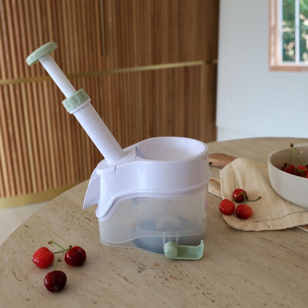 Dénoyauteur à cerises en plastique blanc et vert posé sur table avec cerises fraîches, vue d'ambiance cuisine