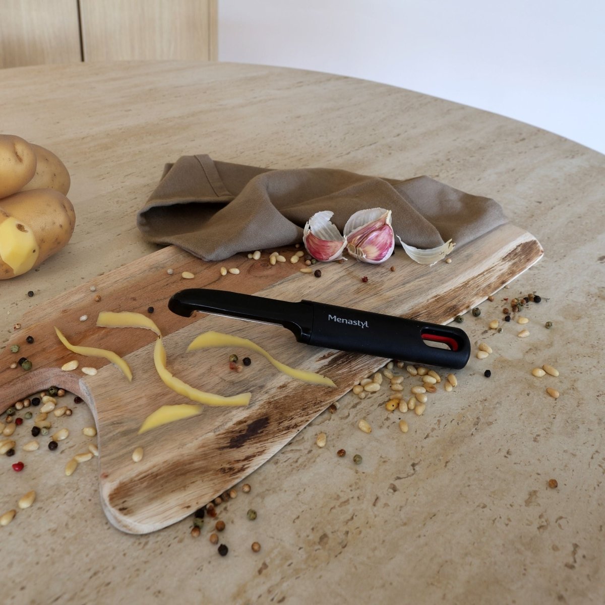 Économe acier inoxydable à manche noir sur planche bois avec pommes de terre, ail et épices