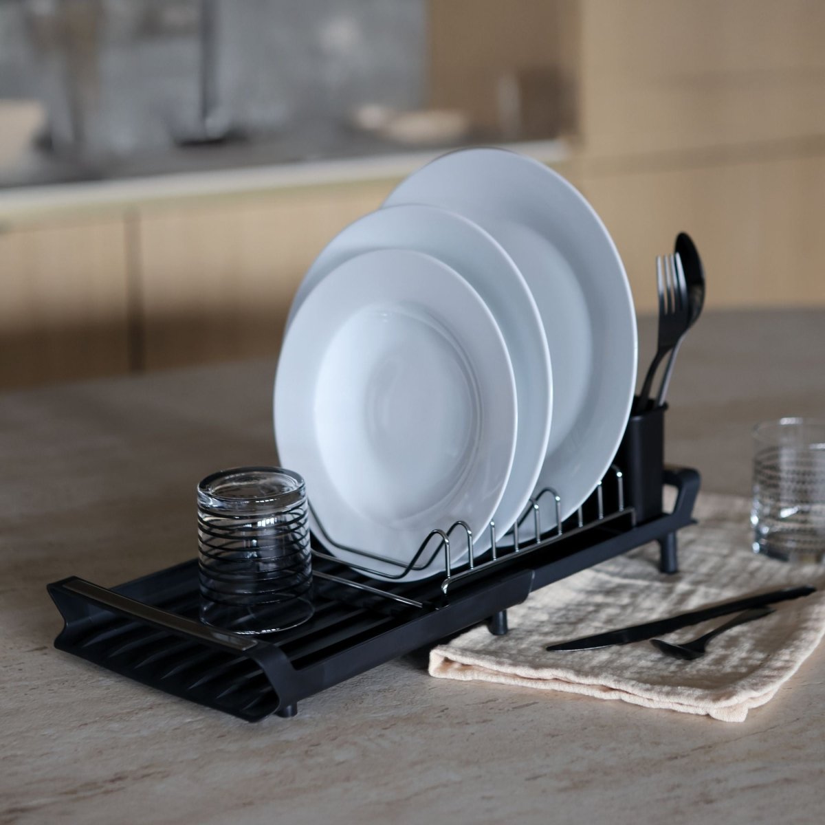 Égouttoir à vaisselle extensible noir avec assiettes blanches et couverts, posé sur plan de travail cuisine