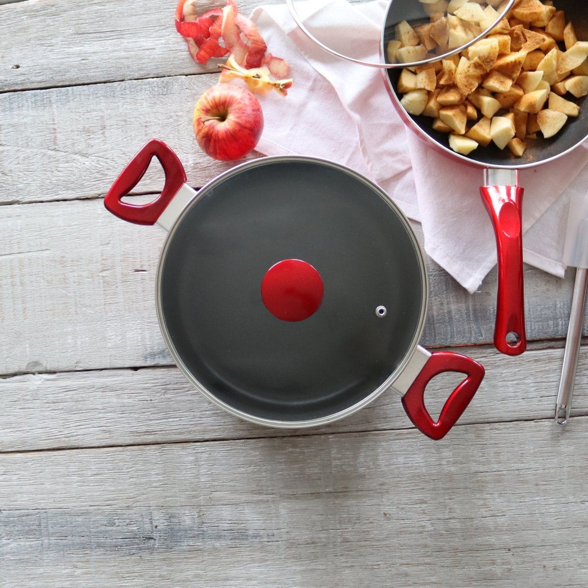 Faitout Cerise 24cm rouge avec couvercle et poignées, préparation de compote de pommes en arrière-plan