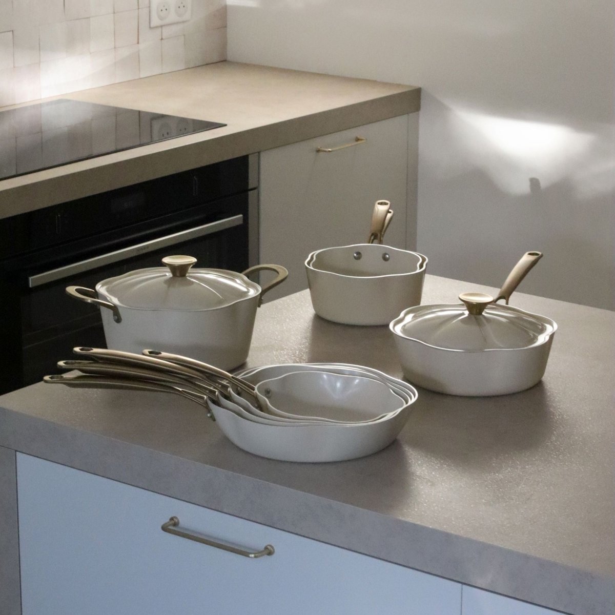 Ensemble gamme Dahlia comprenant faitout 24cm beige, casseroles et poêles en aluminium recyclé sur plan de travail cuisine moderne