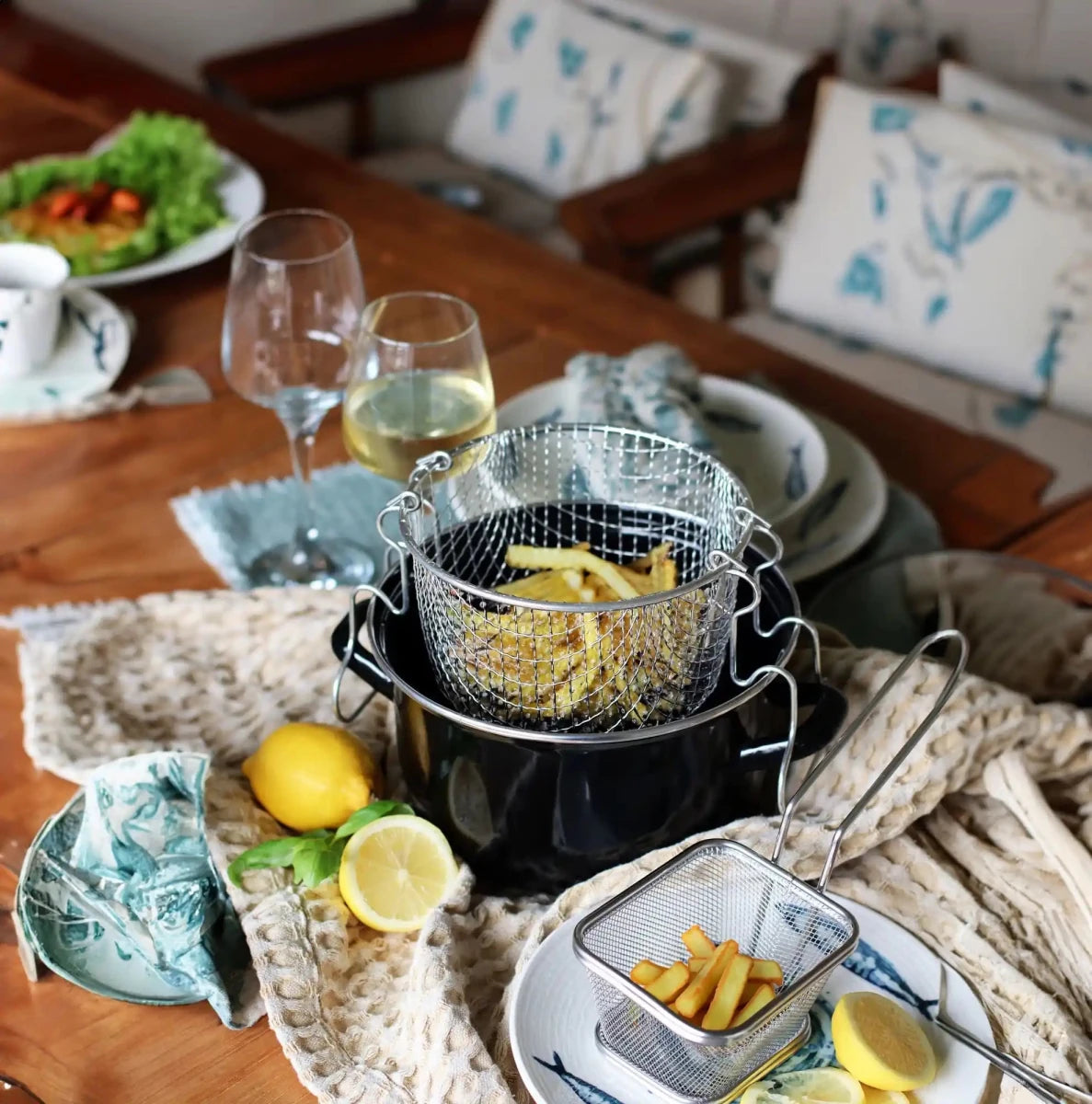 Friteuse en acier émaillé 20 cm avec panier grillagé et frites dorées, mise en scène table avec citron et vin blanc