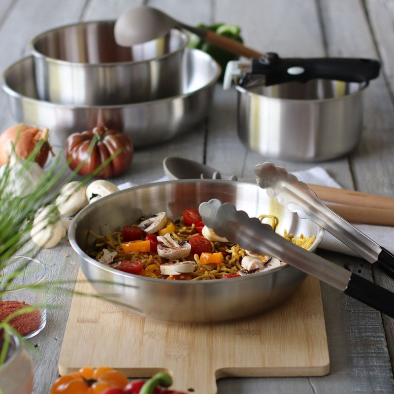 Lot de 3 poêles Iris Inox avec poignée amovible, présentées avec légumes et planche en bois