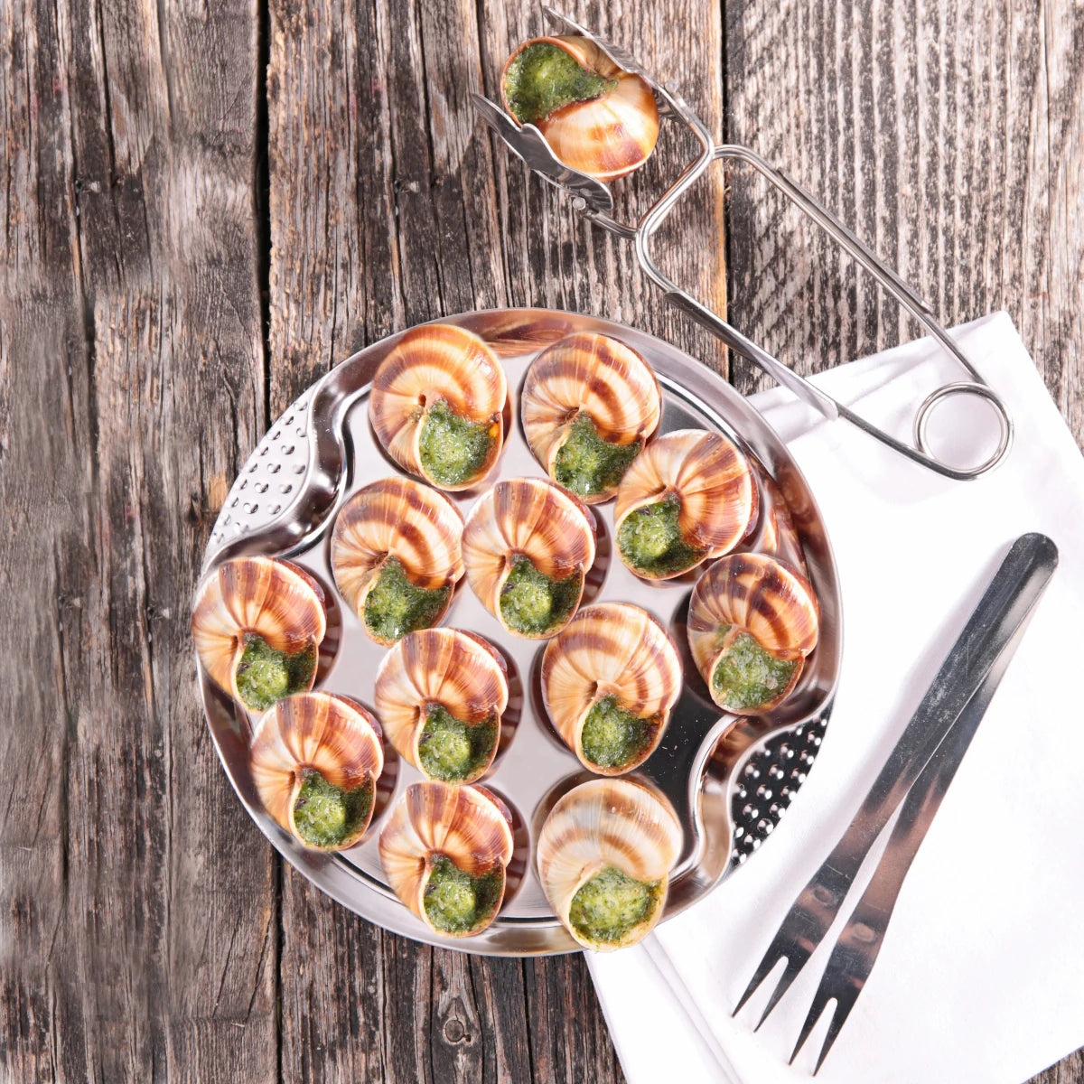 Assiettes à escargots en acier inoxydable garnies d'escargots au beurre persillé, vue de dessus avec ustensiles