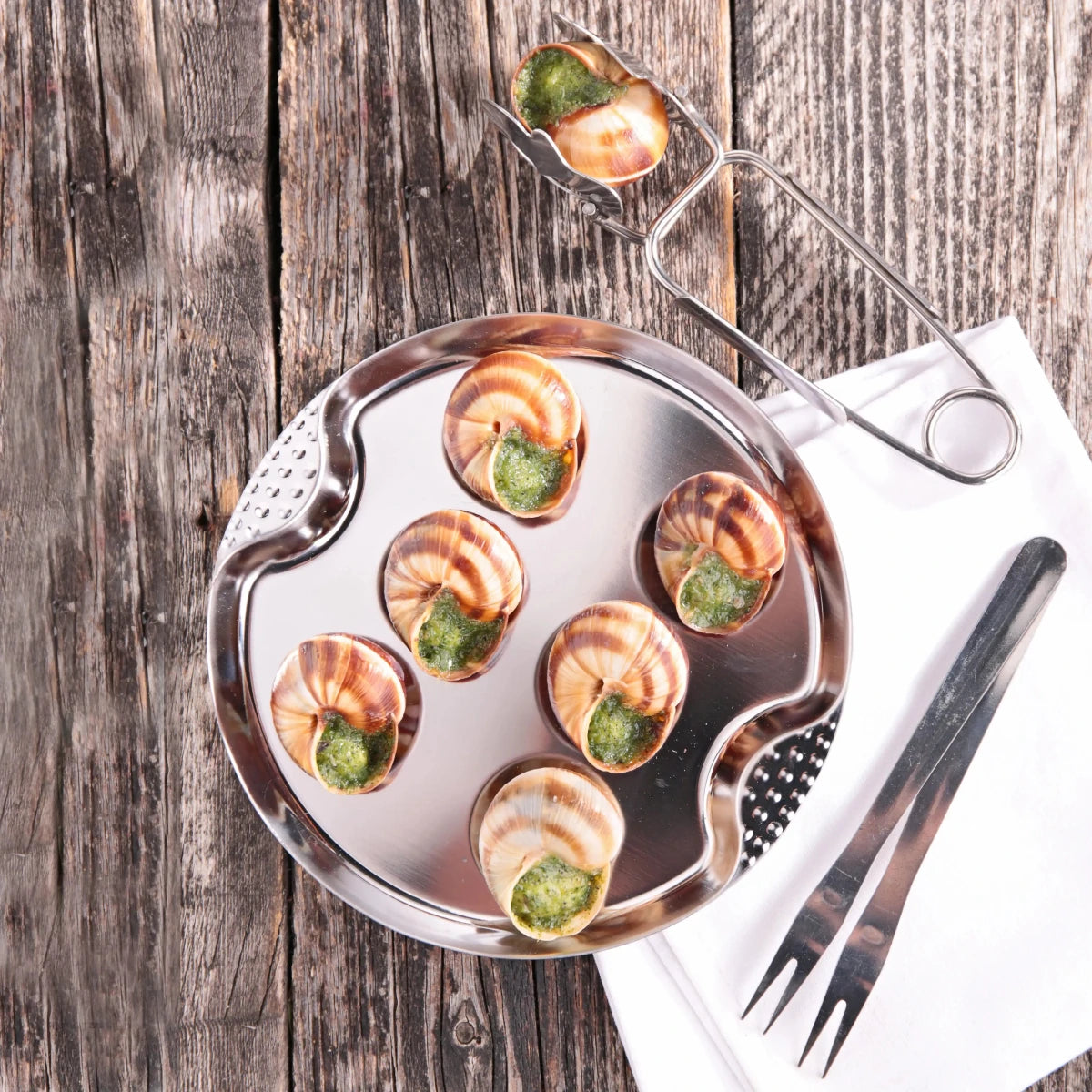 Assiettes à escargots en acier inoxydable garnies de beurre persillé, vue de dessus avec accessoires