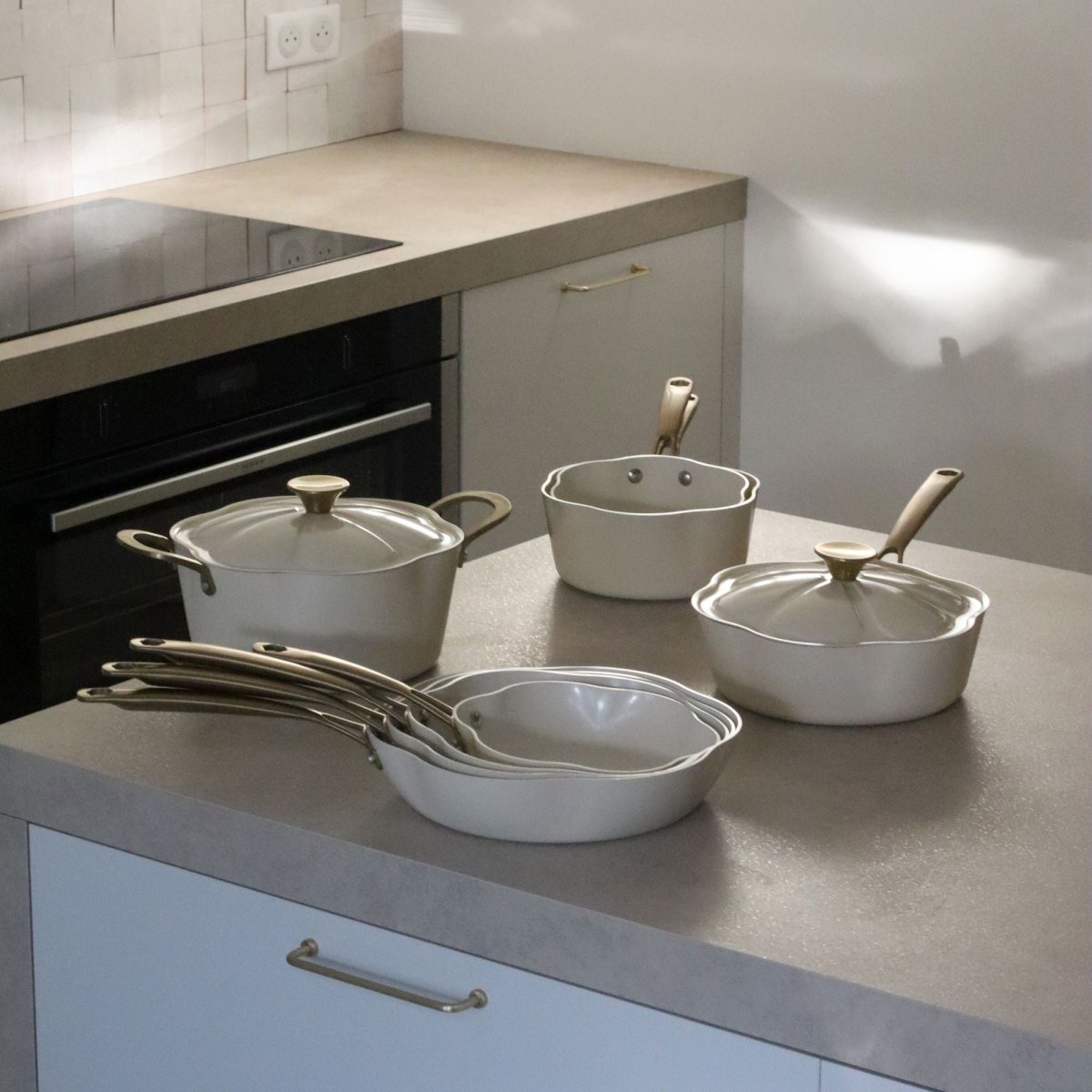 Ensemble de poêles et casseroles Dahlia beige en aluminium recyclé disposées sur plan de travail de cuisine moderne