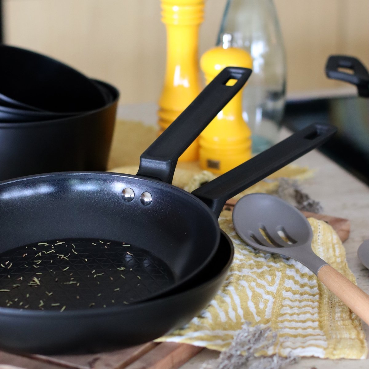 Poêle First 20 cm en aluminium noir et ustensiles de cuisine sur tissu jaune motif zébré