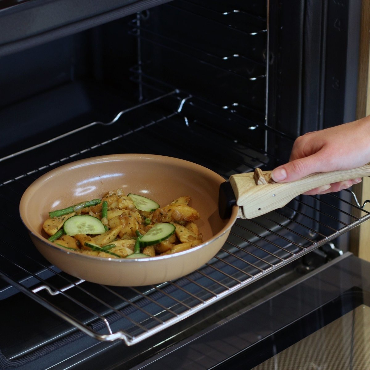 Poignée amovible en bakélite effet bois fixée sur poêle beige sortant du four avec légumes rôtis