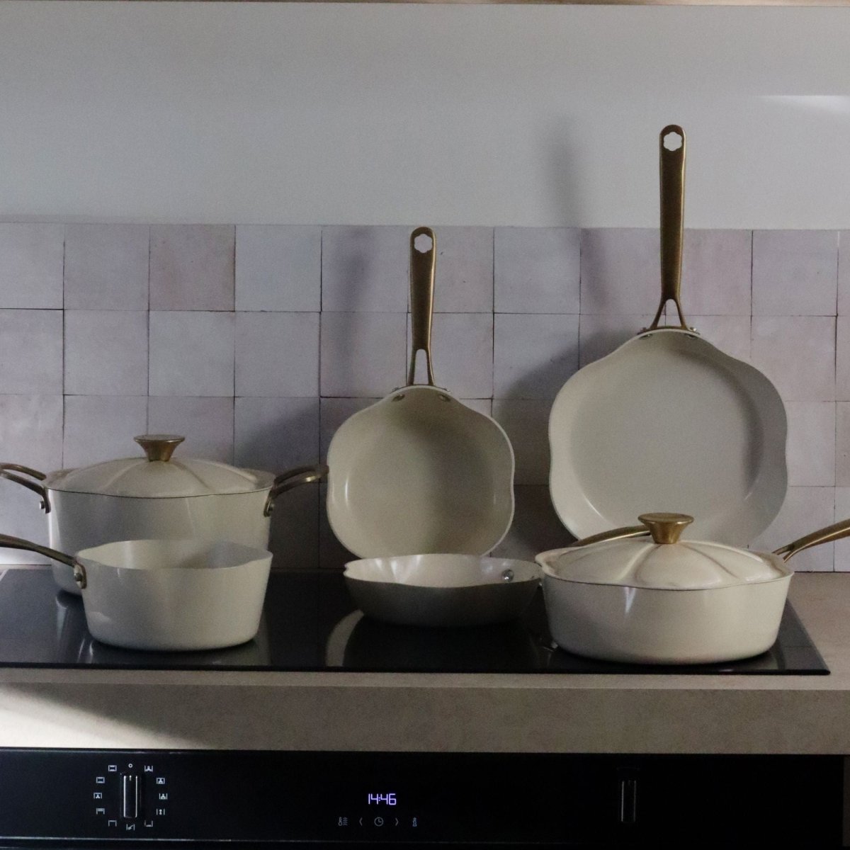 Ensemble d'ustensiles de cuisine Dahlia beige disposés sur plaque induction, avec sauteuse 24 cm au premier plan
