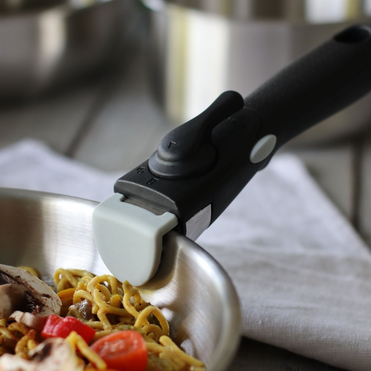 Poignée amovible noire du set Iris Inox clipsée sur casserole en inox, vue rapprochée sur plat de pâtes