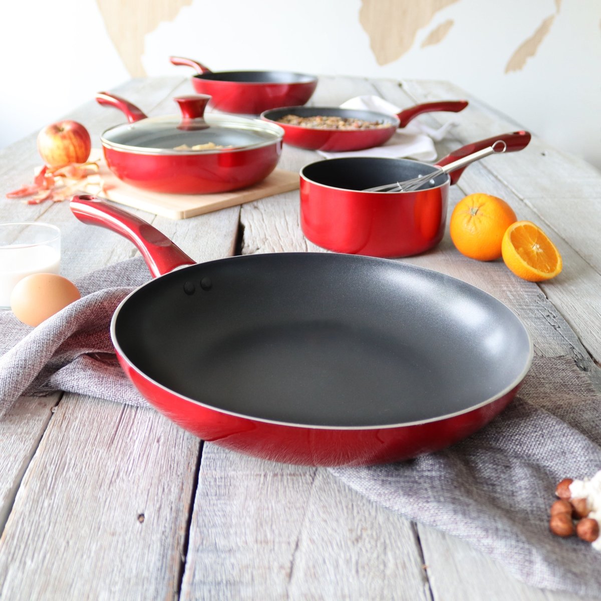 Set de 3 poêles cerise en aluminium 24/28/32 cm avec revêtement antiadhésif noir, disposées sur table en bois blanc avec fruits frais