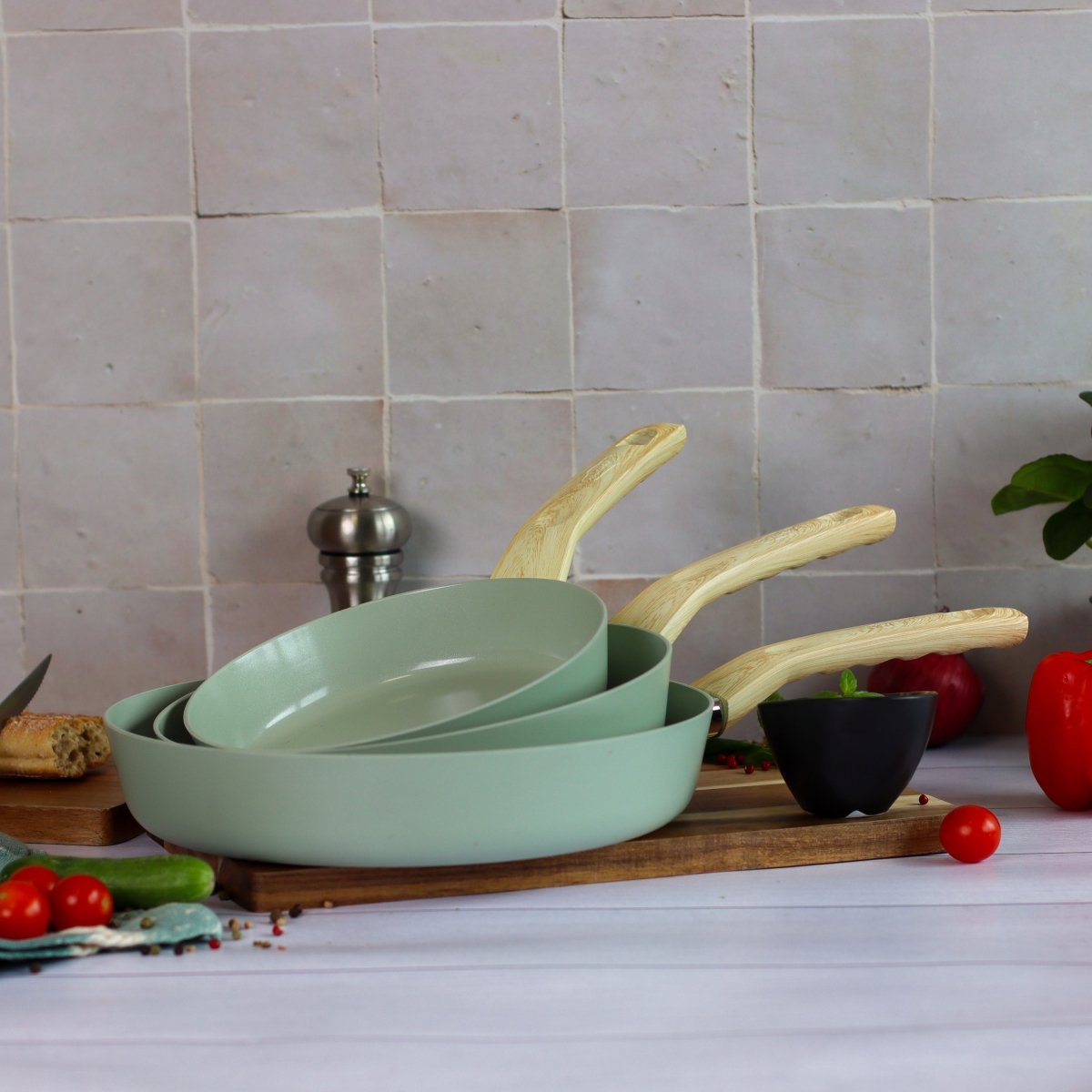 Set de 3 poêles Colorama céladon 20/24/28cm en aluminium avec manches bois, disposées sur planche en bois