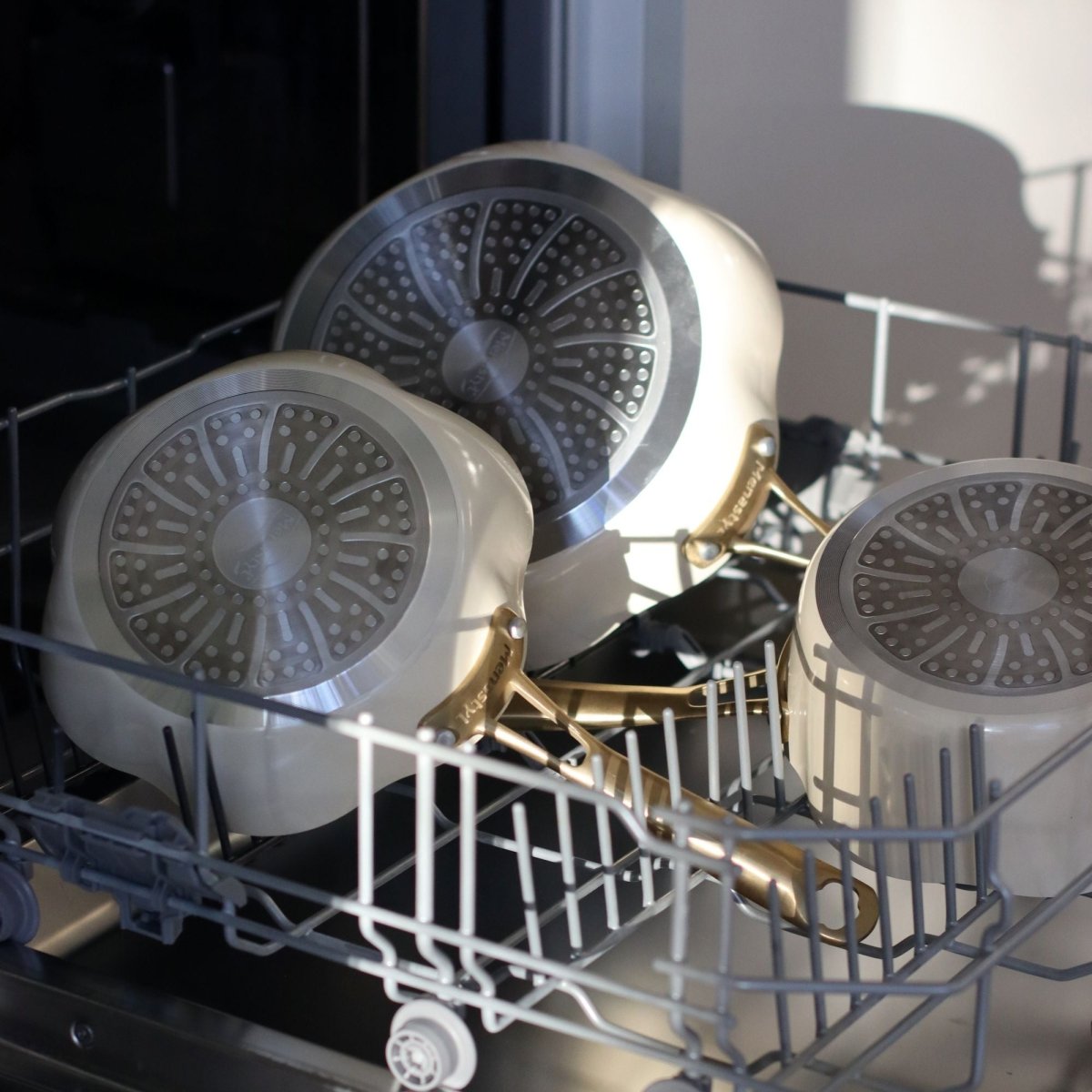 Set de 3 poêles Dahlia beige en aluminium recyclé placées dans un lave-vaisselle ouvert, vue intérieure avec revêtement antiadhésif