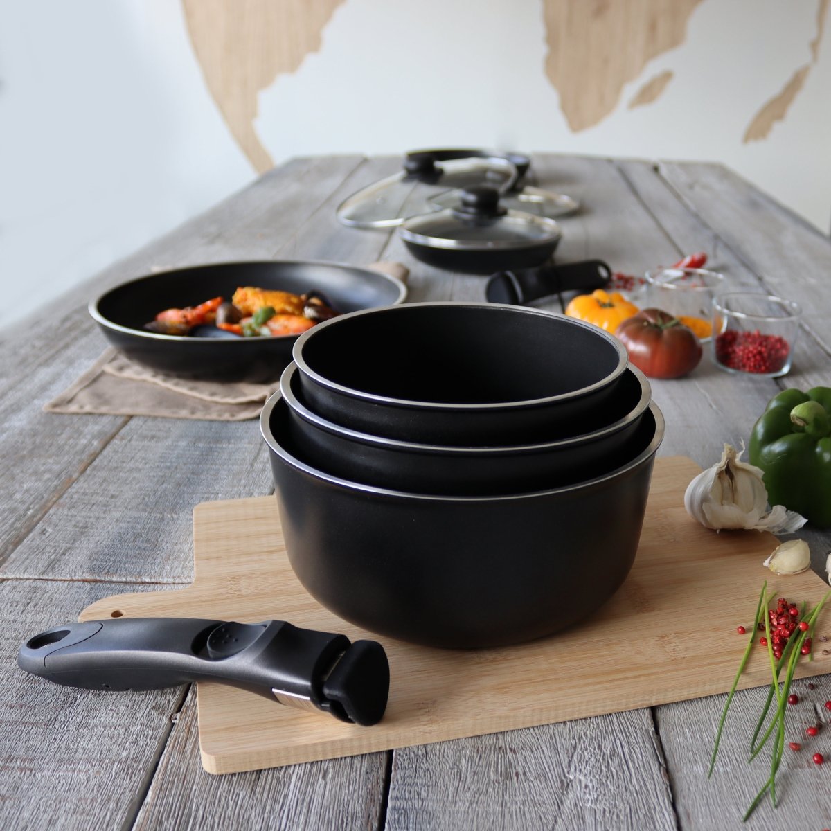 Set de 4 pièces en aluminium noir empilées avec poignée amovible bakélite, sur planche bois avec légumes frais