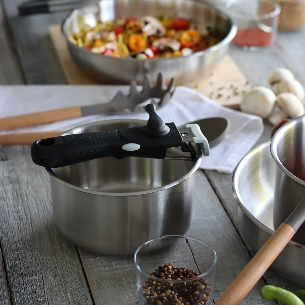 Set de 4 pièces Iris en acier inoxydable avec casserole, poignée amovible et ustensiles de cuisine sur table en bois
