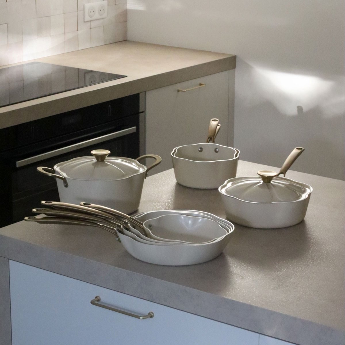 Set de 5 pièces Dahlia en aluminium recyclé beige disposé sur plan de travail cuisine moderne, poêles et casseroles