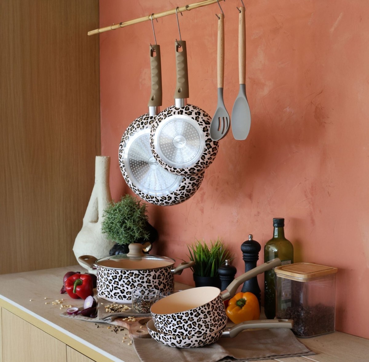 Set de 5 pièces Léopard en aluminium : casseroles, poêles et ustensiles suspendus sur fond terracotta avec légumes frais