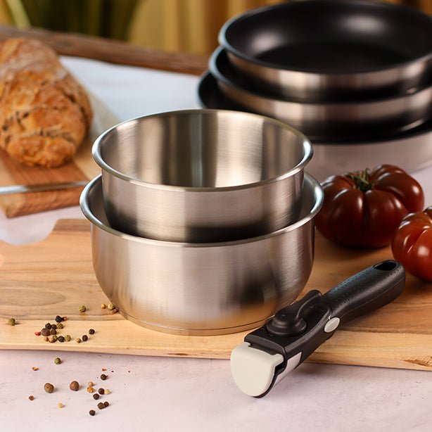 Set de casseroles et poêles en acier inoxydable avec poignée amovible, empilées sur plan de travail bois avec tomates
