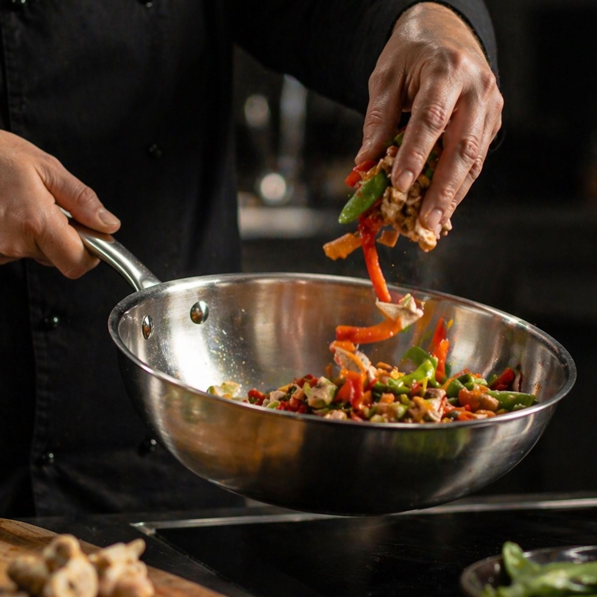 Cuisson de légumes colorés dans wok inox Triply, saisie à la main en action