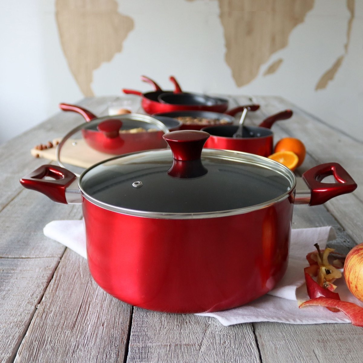Batterie de cuisine aluminium rouge cerise 8 pièces avec couvercles en verre, disposée sur table en bois clair