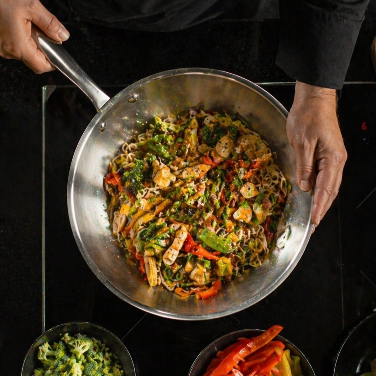 Wok triply acier inoxydable 24cm en pleine cuisson de légumes sautés et nouilles sur plaque à induction