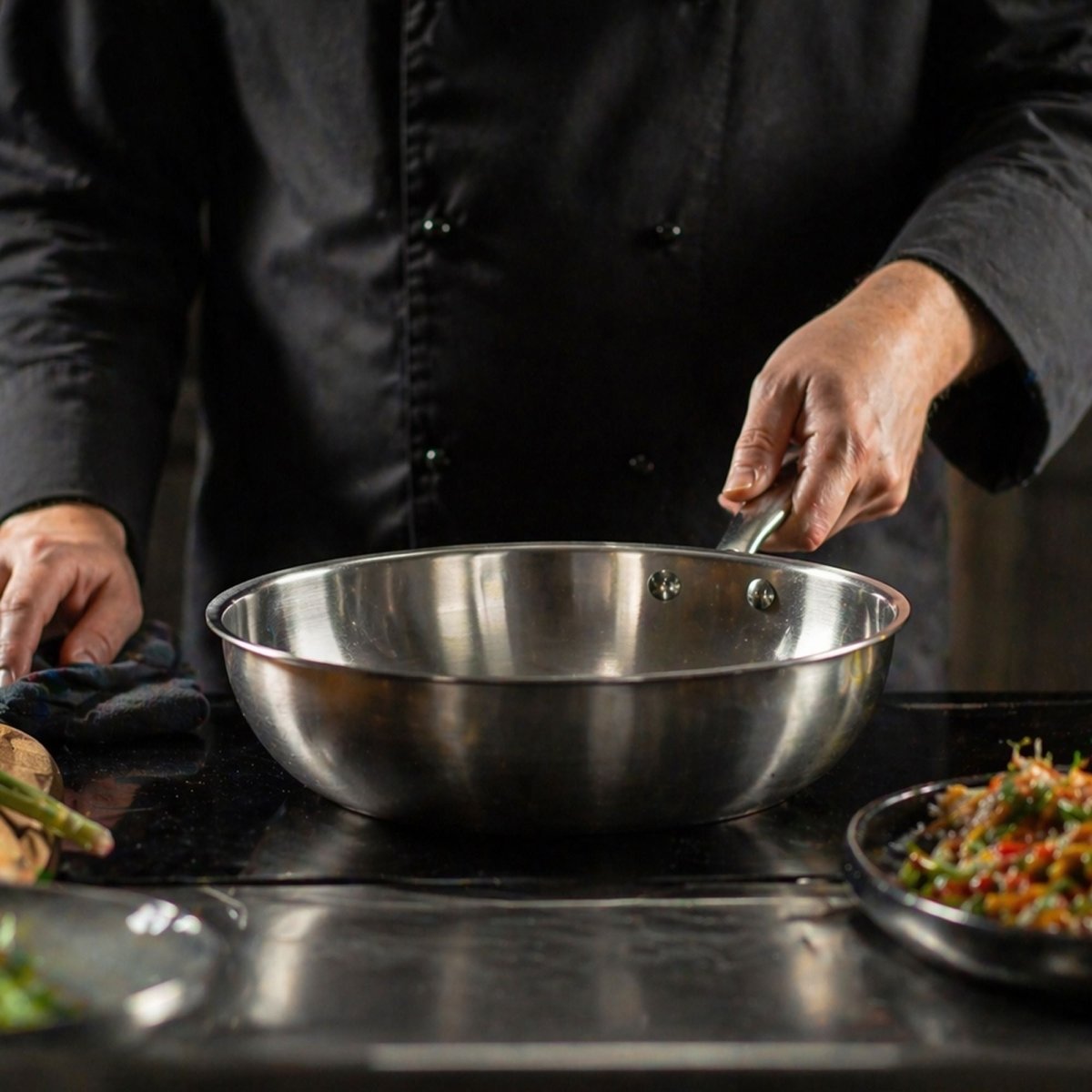 Wok Triply 28cm en acier inoxydable tenu par chef cuisinier, vue détaillée en cuisine professionnelle