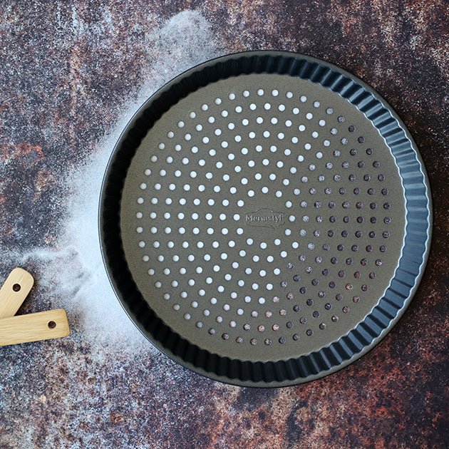 Moule à tarte perforé Amandine 30 cm en acier carbone, vue de dessus sur fond texturé