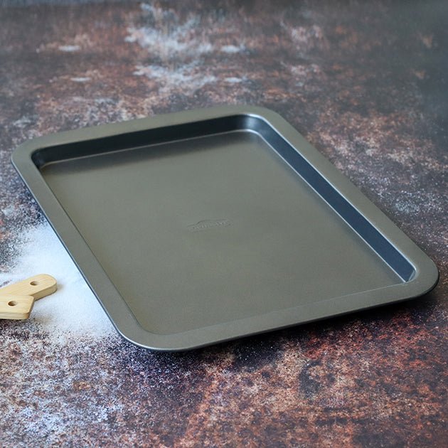 Plaque à four Amandine 38 cm en acier carbone anthracite posée sur fond texturé avec spatule en bois